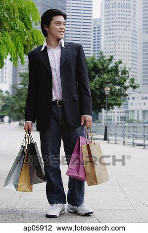 Stock Image - Man standing with shopping bags, looking away. Fotosearch