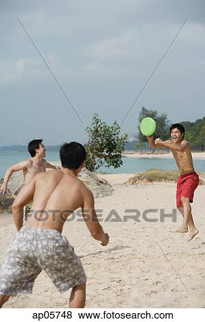 Three men on beach playing with Frisbee View Large Photo Image Stock Photo - Three men on beach playing with Frisbee. Fotosearch