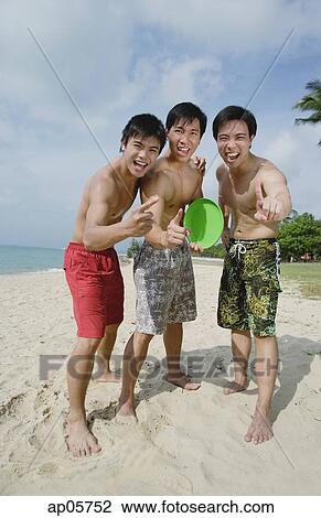 Stock Image - Three men on beach, standing side by side, making hand sign. Fotosearch