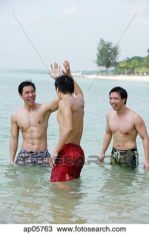 Stock Image - Three men standing waist deep in sea. Fotosearch