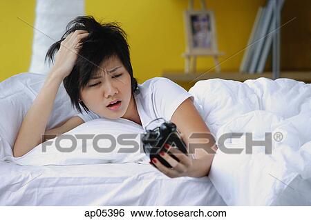 Stock Photograph - Woman in bed, looking at alarm clock. Fotosearch