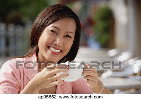 Stock Image - Woman in cafe holding coffee cup, smiling at camera. Fotosearch