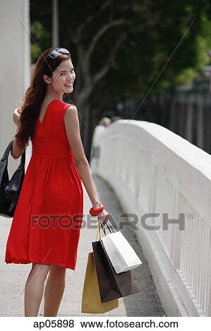 Stock Photo - Woman in red dress carrying shopping bags, looking over shoulder. Fotosearch