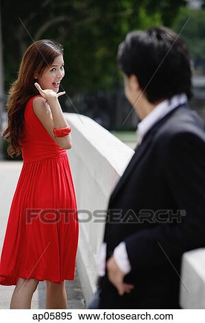 Stock Photography - Woman making hand sign to man in foreground. Fotosearch