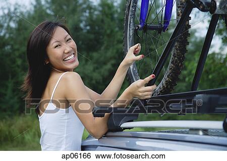 Woman securing bike on top of car, smiling at camera View Large Photo Image Stock Photograph - Woman securing bike on top of car, smiling at camera. Fotosearch