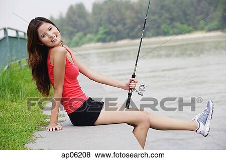 Woman sitting by river, holding fishing rod View Large Photo Image Stock Photo - Woman sitting by river, holding fishing rod. Fotosearch