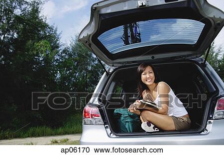 Woman sitting in boot of car, holding magazine View Large Photo Image Stock Image - Woman sitting in boot of car, holding magazine. Fotosearch