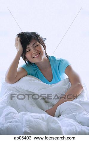 Woman sitting on bed, smiling, eyes closed View Large Photo Image Stock Image - Woman sitting on bed, smiling, eyes closed. Fotosearch