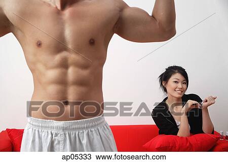 Woman sitting on sofa, filing her nails, man in foreground, flexing muscles View Large Photo Image Stock Image - Woman sitting on sofa, filing her nails, man in foreground, flexing muscles. Fotosearch