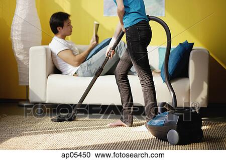 Woman vacuuming, man sitting on sofa reading magazine View Large Photo Image Stock Image - Woman vacuuming, man sitting on sofa reading magazine. Fotosearch