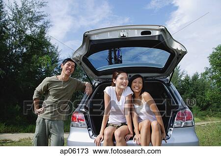 Women sitting in boot of car, man leaning on car View Large Photo Image Stock Image - Women sitting in boot of car, man leaning on car. Fotosearch