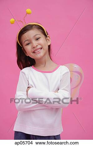 Picture - Young girl wearing fairy wings and deely bopper, arms crossed. Fotosearch