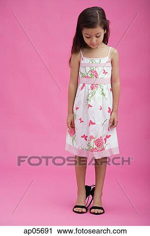 Stock Image - Young girl wearing high heel shoes, looking down. Fotosearch