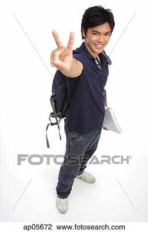 Stock Image - Young man carrying books and a backpack, making peace sign. Fotosearch