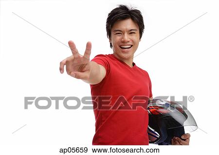 Young man carrying helmet, making peace sign View Large Photo Image Stock Photo - Young man carrying helmet, making peace sign. Fotosearch