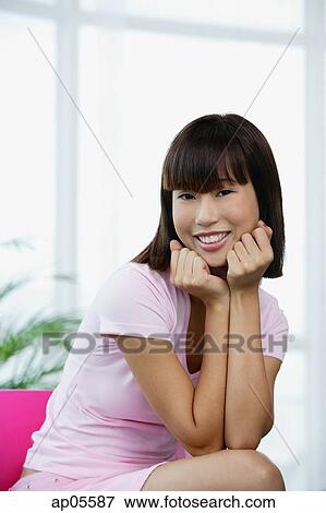Stock Photo - Young woman dressed in pink, sitting on pink chair, hands on chin. Fotosearch