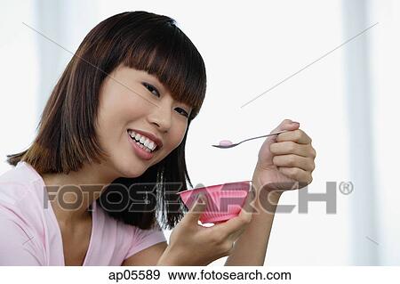 Stock Photo - Young woman eating from pink bowl. Fotosearch