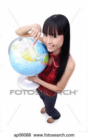Young woman holding and pointing at globe, smiling at camera View Large Photo Image Stock Photo - Young woman holding and pointing at globe, smiling at camera. Fotosearch