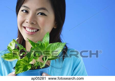 Stock Image - Young woman holding plant pot, portrait. Fotosearch