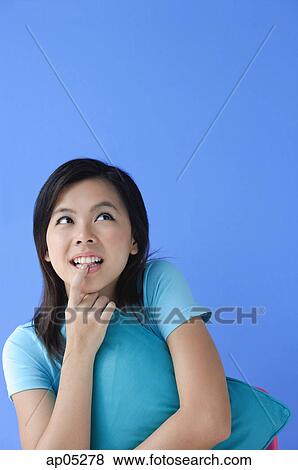 Stock Photo - Young woman hugging pillow, biting finger. Fotosearch
