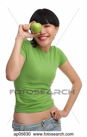 Stock Image - Young woman in green T-shirt with green apple. Fotosearch