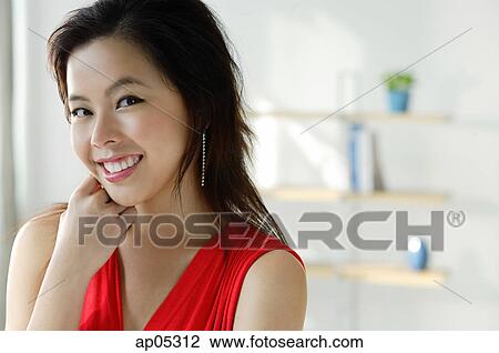 Stock Image - Young woman in red top, smiling at camera. Fotosearch