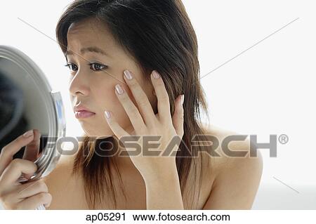 Young woman looking at mirror, touching her face View Large Photo Image Stock Image - Young woman looking at mirror, touching her face. Fotosearch