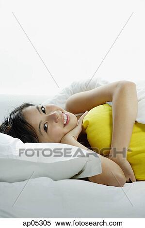 Stock Photography - Young woman lying on bed, embracing pillow. Fotosearch