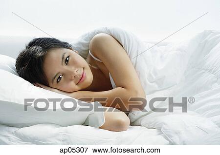 Young woman lying on bed, looking at camera View Large Photo Image Stock Photo - Young woman lying on bed, looking at camera. Fotosearch