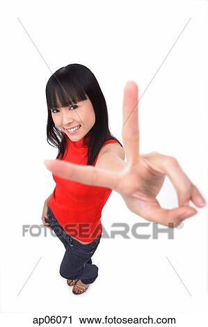 Stock Image - Young woman making peace sign at camera. Fotosearch