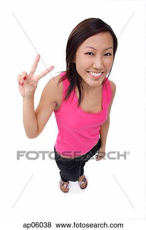 Young woman making peace sign, smiling up at camera View Large Photo Image Stock Photo - Young woman making peace sign, smiling up at camera. Fotosearch