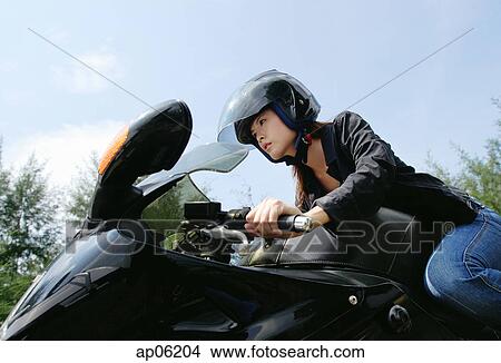 Picture - Young woman riding motorbike, low angle view. Fotosearch