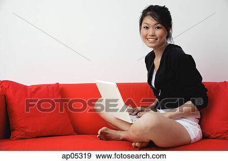 Young woman sitting on sofa, with laptop, smiling at camera View Large Photo Image Stock Photo - Young woman sitting on sofa, with laptop, smiling at camera. Fotosearch