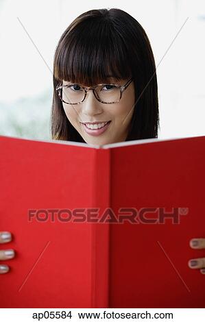 Picture - Young woman smiling at camera, holding book. Fotosearch