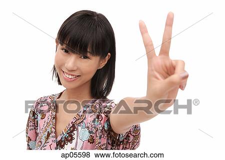 Stock Photo - Young woman smiling at camera, making peace sign. Fotosearch