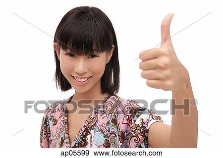 Stock Photo - Young woman smiling at camera, making thumbs-up sign. Fotosearch