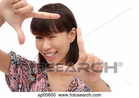 Stock Image - Young woman smiling at camera through finger frame. Fotosearch