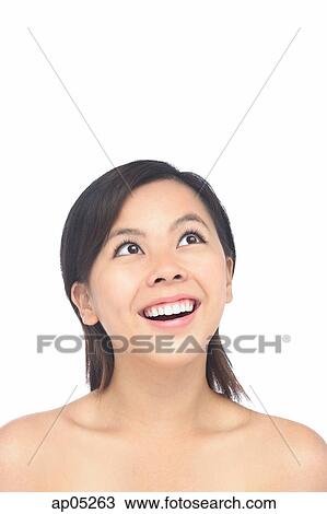 Stock Image - Young woman smiling, looking up, head shot. Fotosearch