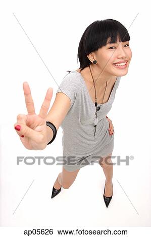 Young woman smiling up at camera, making peace sign View Large Photo Image Stock Photograph - Young woman smiling up at camera, making peace sign. Fotosearch