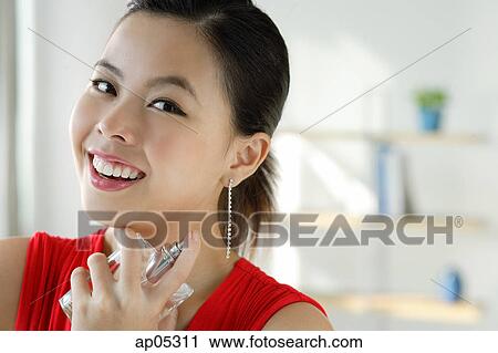 Young woman spraying perfume, smiling at camera View Large Photo Image Stock Image - Young woman spraying perfume, smiling at camera. Fotosearch