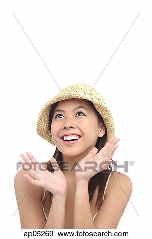 Stock Photo - Young woman wearing hat, looking up, smiling. Fotosearch