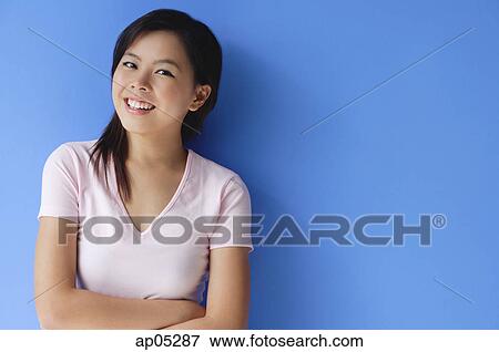 Young woman with arms crossed, standing against blue background View Large Photo Image Stock Photo - Young woman with arms crossed, standing against blue background. Fotosearch