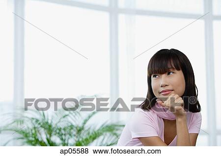 Stock Photo - Young woman with hand on chin, looking away. Fotosearch