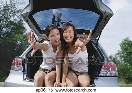 Young women sitting in boot of car, reaching towards camera View Large Photo Image Stock Photography - Young women sitting in boot of car, reaching towards camera. Fotosearch