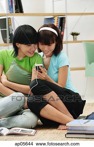 Young women wearing earphones, listening to MP3 player View Large Photo Image Picture - Young women wearing earphones, listening to MP3 player. Fotosearch