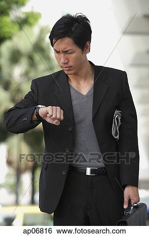 Businessman holding briefcase, looking at watch, frowning View Large Photo Image Stock Photograph - Businessman holding briefcase, looking at watch, frowning. Fotosearch
