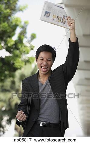 Businessman holding newspaper in air, smiling View Large Photo Image Stock Photo - Businessman holding newspaper in air, smiling. Fotosearch