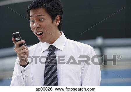 Stock Photograph - Businessman looking at mobile phone, making a face. Fotosearch