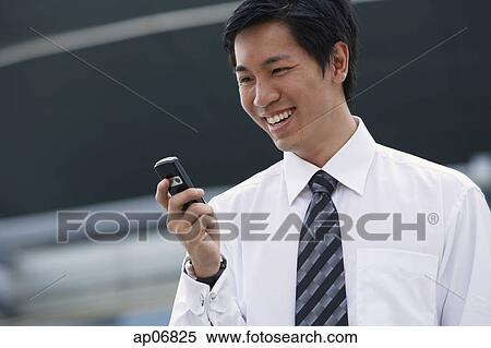 Businessman looking at mobile phone, smiling View Large Photo Image Stock Photography - Businessman looking at mobile phone, smiling. Fotosearch