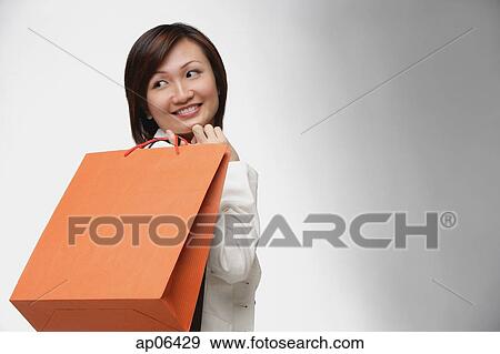 Stock Photo - Businesswoman carrying shopping bags, looking over shoulder. Fotosearch